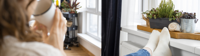 Vrouw zit met voeten tegen de verwarming een kopje koffie te drinken