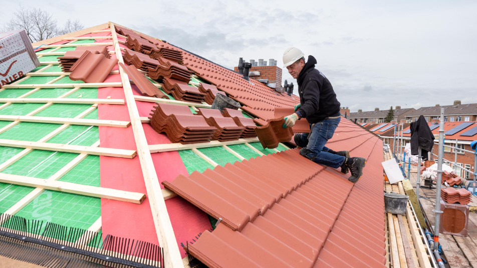 Een dakdekker brengt isolatie aan en legt nieuwe dakpannen op het dak van een woning